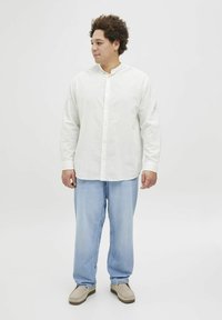 Weißes Hemd mit Stehkragen, kombiniert mit hellblauen, lässigen Hosen und beigen Slippern. Glattes, strukturiertes Material.