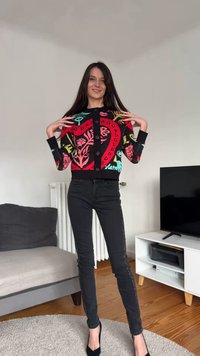 Colorful black cardigan with floral and heart patterns, featuring a button closure. Paired with black jeans with side embellishments.