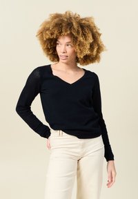 Svart v-ringad tröja med långa ärmar. Strukturerad stickad detaljer på ärmarna. Matchad med ljusa byxor. Slät tygfinish.