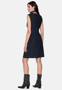 Marineblaues ärmelloses Kleid mit figurbetonter Silhouette, kontrastierenden Nähten, Reißverschluss auf der Rückseite und kombiniert mit schwarzen Cowboy-Stiefeln.