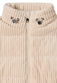 Chaleco con cremallera de color crema con textura acanalada vertical, cuello alto y ajustadores laterales para ajuste. Tejido suave y aterciopelado con cremallera lisa.