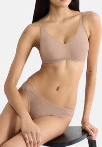Reggiseno leggero nude con coppe triangolari e sottili spalline regolabili, abbinato a slip a vita bassa coordinati. Tessuto liscio, cuciture minime.