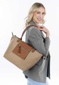 Borsa tote in nylon beige con dettagli in pelle marrone, dotata di tasca frontale con zip, manici doppi e cuciture a contrasto.