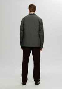 Grå isolert jakke med krage, vist fra baksiden, paret med mørkebrune bukser og svarte sko, mot en enkel bakgrunn.