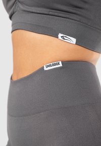 Close-up van de taille van een persoon die grijze geribbelde hoge taille leggings en een bijpassend crop top draagt met SMILODOX-merklabels.