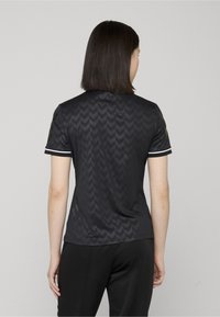 T-shirt de sport noir à manches courtes avec un motif en chevron, comportant des accents blancs sur le col et les manches, fabriqué dans un matériau lisse et extensible.
