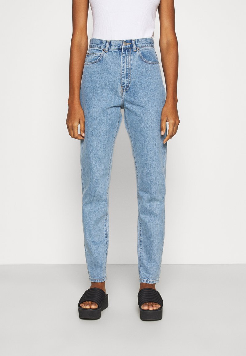 Jeans claros de cintura alta com corte reto. Feitos de denim com um design clássico de cinco bolsos. Sandálias pretas de plataforma com tiras ribadas.