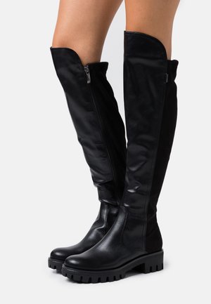 Bottes noires montant jusqu'aux genoux avec une tige en cuir lisse et élégant, fermeture éclair sur le côté, et semelle en caoutchouc texturée avec des crampons profonds.