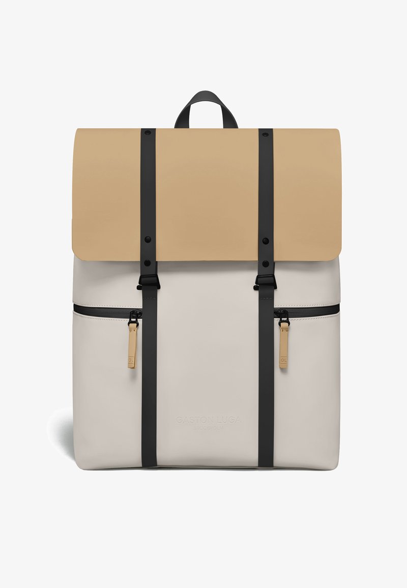 Sac à dos Gaston Luga beige et crème avec des bretelles verticales noires, deux poches avant zippées et une poignée supérieure.