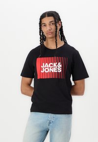 Mustapaita, jossa on rohkea punainen ja valkoinen "JACK&JONES" -logo pystysuorilla viivoilla. Lyhyet hihat ja klassinen pyöreä kaula-aukko.