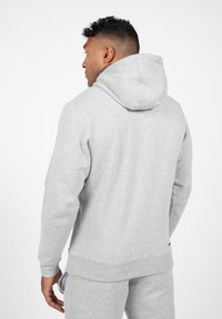 Lichte grijze hoodie van zacht materiaal, met een trekkoordcapuchon en ribbels aan de mouwen. Inclusief een zak en een klein logo aan de zoom.