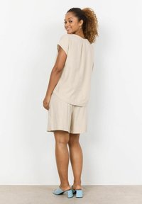 Beige Leinenoberteil mit kurzen Ärmeln und Rückenfalte, kombiniert mit beigen Shorts. Abgerundet mit hellblauen, hochhackigen Mules. Einfacher und lässiger Schnitt.