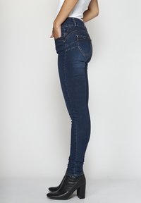 Mörkblå skinny jeans med hög midja, med dekorativ sömnad, bakfickor och en slät textur. Bärs med svarta klackboots.