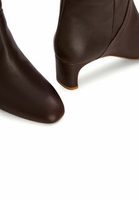 Hnědé kožené kotníkové boty s špičatou špičkou a nízkým, zúženým podpatkem. Hladký povrch a jemný lesk, se bezešvou konstrukcí.