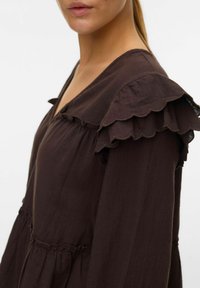 Blouse marron avec un col en V, un col en dentelle froncé, des détails froncés et un tissu doux et texturé.