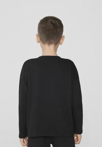 Czarna koszula z długim rękawem, okrągłym dekoltem, luźnym krojem i miękką teksturą. Posiada obniżone ramiona i wykończone mankiety.