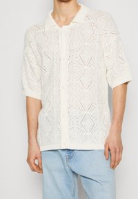Witte gebreide cardigan met korte mouwen, voorzien van een ruitpatroon, knoopsluiting en een zachte kraag. Geweven, luchtige stof.