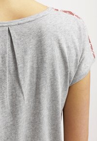 Grijze T-shirt met korte mouwen en een plooi detail aan de achterkant, met patroonaccenten in bordeauxrood op de schouders. Zacht, lichtgewicht materiaal.