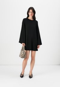 Vestido negro de manga larga con un corte holgado. Combinado con un bolso de piel de serpiente y zapatos negros de punta. Diseño simple y moderno.