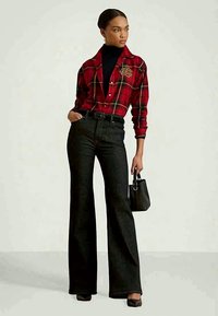 Γυναίκα ντυμένη με κόκκινο καρό πουκάμισο πάνω από μαύρο ζιβάγκο, μαύρο ψηλόμεσο παντελόνι σε φαρδιά γραμμή, μαύρα παπούτσια, κρατώντας μια μικρή μαύρη τσάντα.