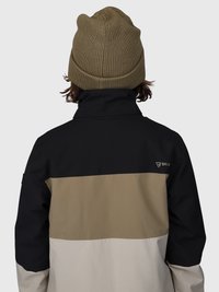 Persona che indossa una giacca a blocchi di colore nero, beige e marrone chiaro con un piccolo logo, e un berretto di maglia verde oliva, vista da dietro.