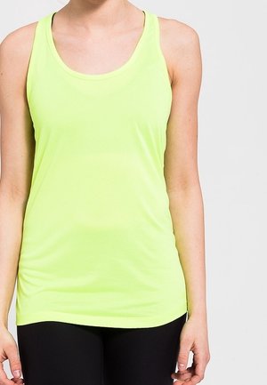 Femme portant un débardeur de sport sans manches jaune vif et un legging noir, debout devant un fond clair uni.