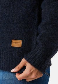 Donker marineblauwe gebreide sweater van textuurwol, met een geribbelde zoom en manchetten, voorzien van een vierkant leren label van Swedemount aan de zijkant.