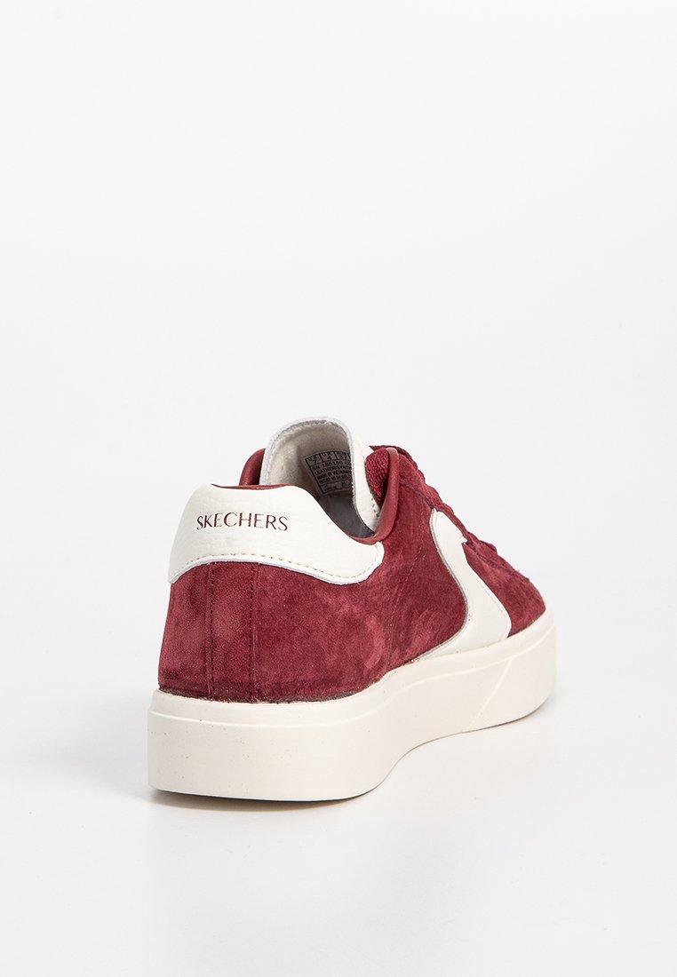 Sneaker rossa in suede con accenti crema, dotata di punta rotonda e una spessa suola bianca. Branding visibile sul tallone. Texture liscia complessiva.