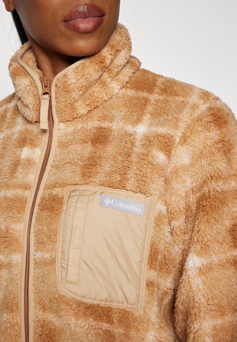 Giacca in pile color beige con una finitura morbida e strutturata e un collo alto. Presenta una chiusura a zip e una tasca sul petto con una toppa del logo.