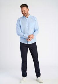 Jasnoniebieska koszula z długim rękawem, z kieszenią na piersi i białymi guzikami, zestawiona z granatowymi spodniami i białymi trampkami.