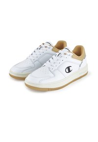 Zapatillas blancas de material de cuero, con punta redonda y suela de goma. Presentan detalles en color beige alrededor del cuello y un logo negro en el costado.