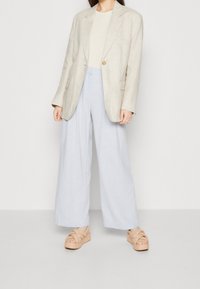 Béžový lněný blazer přes světle béžový top, spárovaný s širokými světle modrými kalhotami a masivními béžovými sandály s pleteným designem.