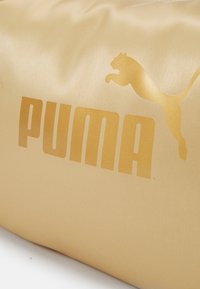 Guldfarvet Puma-taske med en glat, shiny overflade. Har et stort, præget logo og et springende katte grafik. rektangulær form.