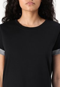 Czarny T-shirt z krótkim rękawem z teksturowanym, wzorzystym mankietem. Gładki materiał z klasycznym okrągłym dekoltem, bez dodatkowych ozdób.