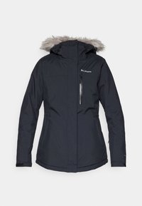 Veste d’hiver noire isolée avec capuche bordée de fourrure, fermeture éclair devant, poches latérales, poche poitrine zippée et logo Columbia sur la poitrine.