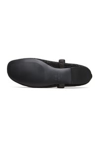 Suela de zapato negra con un patrón de agarre texturizado, que presenta un borde liso y una correa elástica para mayor ajuste y soporte.