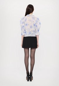 Jasnoniebieska kurtka w kwiatowy wzór z bufkami, z kołnierzem, zestawiona z czarną rozkloszowaną spódnicą i czarnymi wysokimi obcasami.