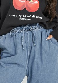 Svart sweatshirt med en grafisk bild av röda äpplen, i kombination med ljusblå jeansbyxor med dragsko som har elastisk midja och sidofickor.