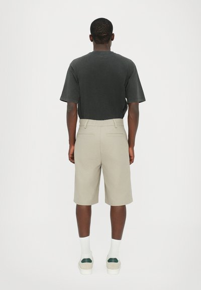 T-shirt noir à manches courtes avec une coupe décontractée, associé à un short beige à mi-cuisses, doté d'une taille élastique et de poches arrière.