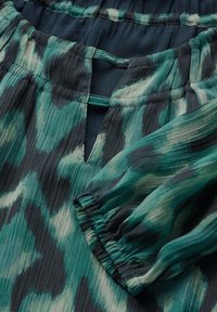 Musterbluse in Grün mit plissierter Textur, featuring einen Schlüssel-ausschnitt und geraffte Ärmelbündchen, aus leichtem Stoff gefertigt.