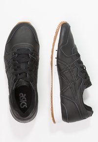 Black lace-up sneakers with leather upper, white midsole, and gum rubber outsole. Features stitching details and ASICS logo on insole.