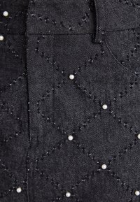 Tissu en denim noir présentant des motifs losanges matelassés et de petits accents en perles blanches. La couture est bien visible sur l'ensemble du design.