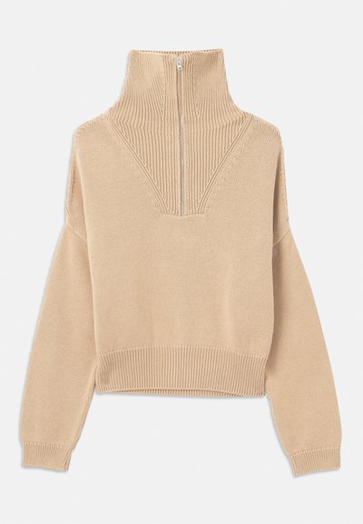 Suéter de punto beige con cuello alto, cierre de media cremallera y hombros caídos. Puños y dobladillo acanalados con un patrón de texturas en el cuerpo.