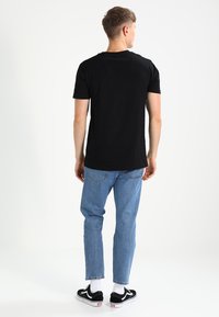 T-shirt noire à manches courtes avec un col rond, associée à un jean en denim bleu clair et des baskets noires avec des semelles blanches.
