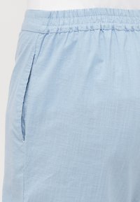 Pantalones cortos azul claro hechos de tela texturizada, con cinturilla elástica y bolsillos laterales. El diseño es simple y funcional.