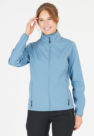 Softshell-jacka i ljusblått med hög krage, dragkedjestängning och två fickor med dragkedja på sidorna. Har en mjuk textur och elastiska ärmslut.