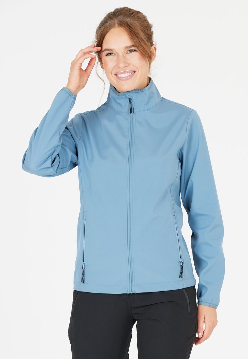 Veste softshell bleu clair avec col haut, fermeture éclair et deux poches latérales zippées. Présente une texture lisse et des poignets élastiques.