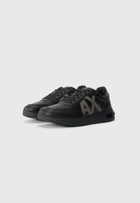 Baskets noires en cuir, avec une surface texturée, des lacets, un col rembourré et un audacieux logo gris "AX" sur le côté.