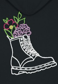 Lo sfondo nero presenta un stivale da combattimento ricamato di bianco con elementi floreali, inclusi fiori rosa e viola e foglie verdi, sui lati.