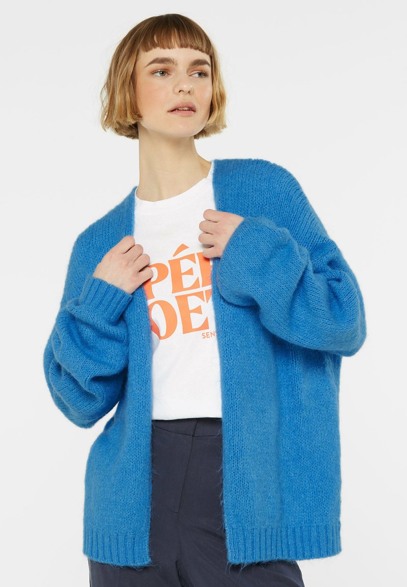 Blau gestrickte Strickjacke mit langen Ärmeln und offenem Design, aus weichem Material gefertigt. Rippbündchen und Saum verleihen Textur.